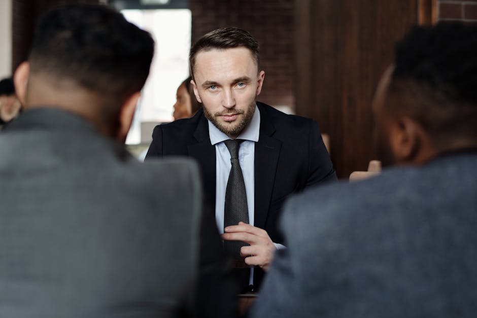 Three men in suits engaged in a serious business meeting indoors.